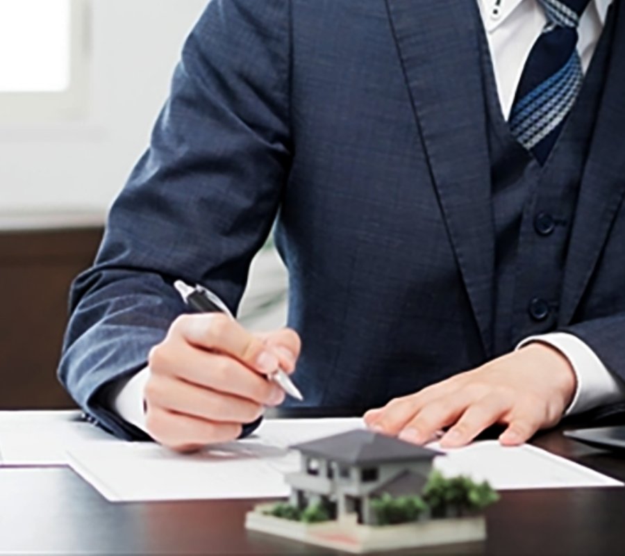 スーツ姿の人物が住宅模型の前で契約書に署名している様子