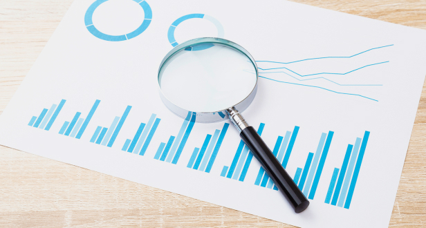 棒グラフと円グラフが描かれた資料の上に虫眼鏡が置かれている